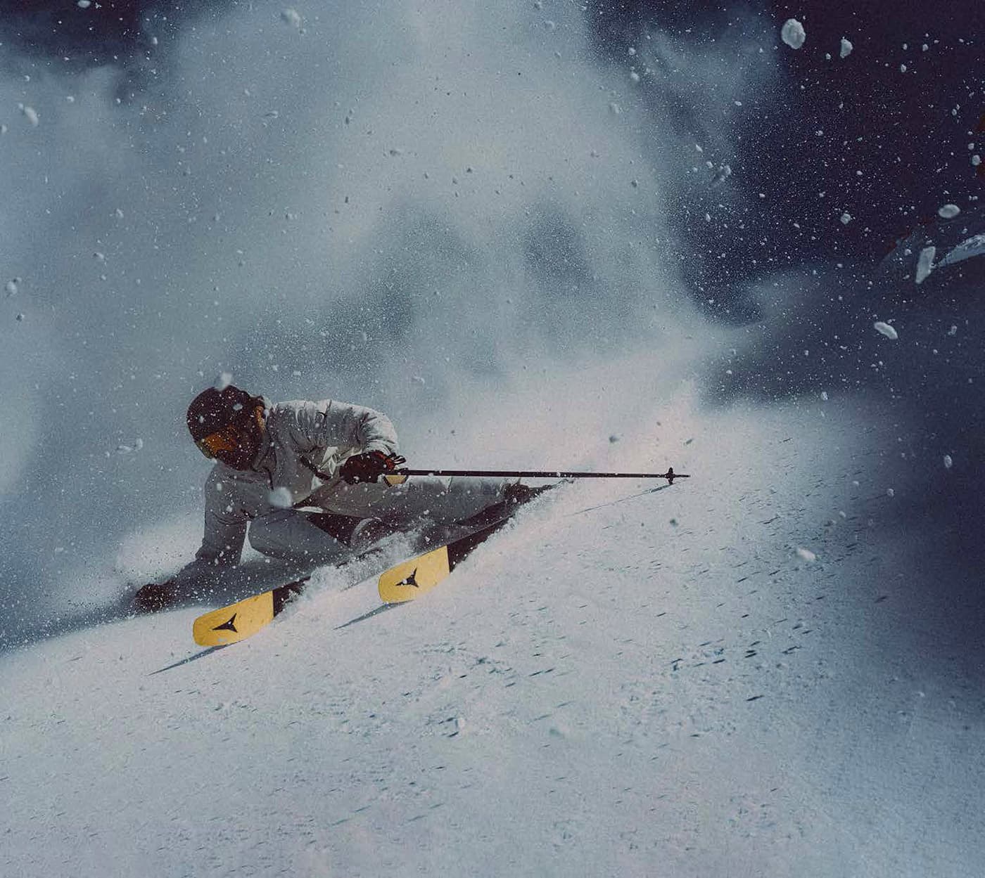 Skier carving through powder on Atomic Maverick skis with yellow tips.