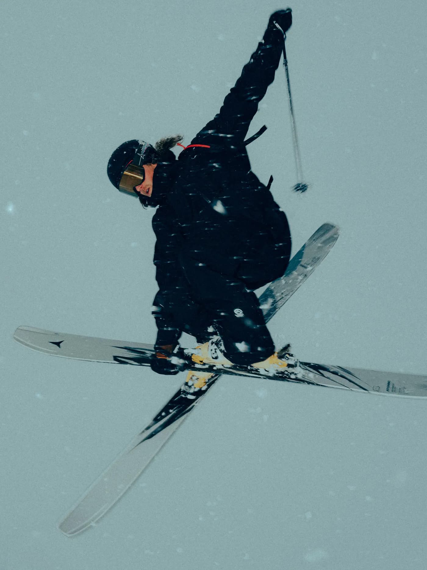 Skier in black outerwear performing a trick on Atomic Maverick skis, showing the grey and black brushstroke-style graphic