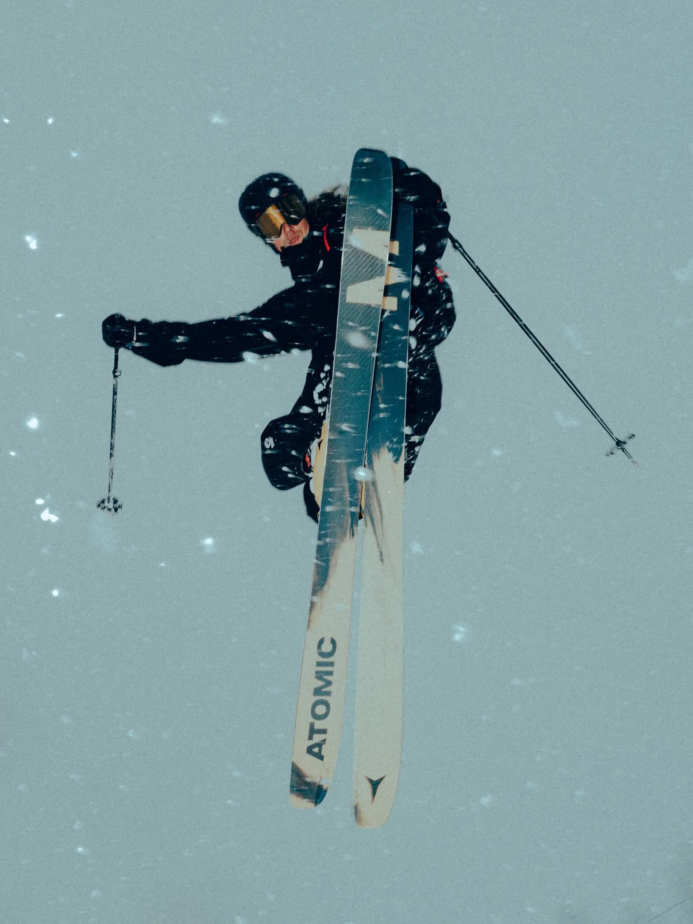 Skier in black outerwear jumping on Atomic Maverick skis, with the grey topsheet and black ski graphic visible