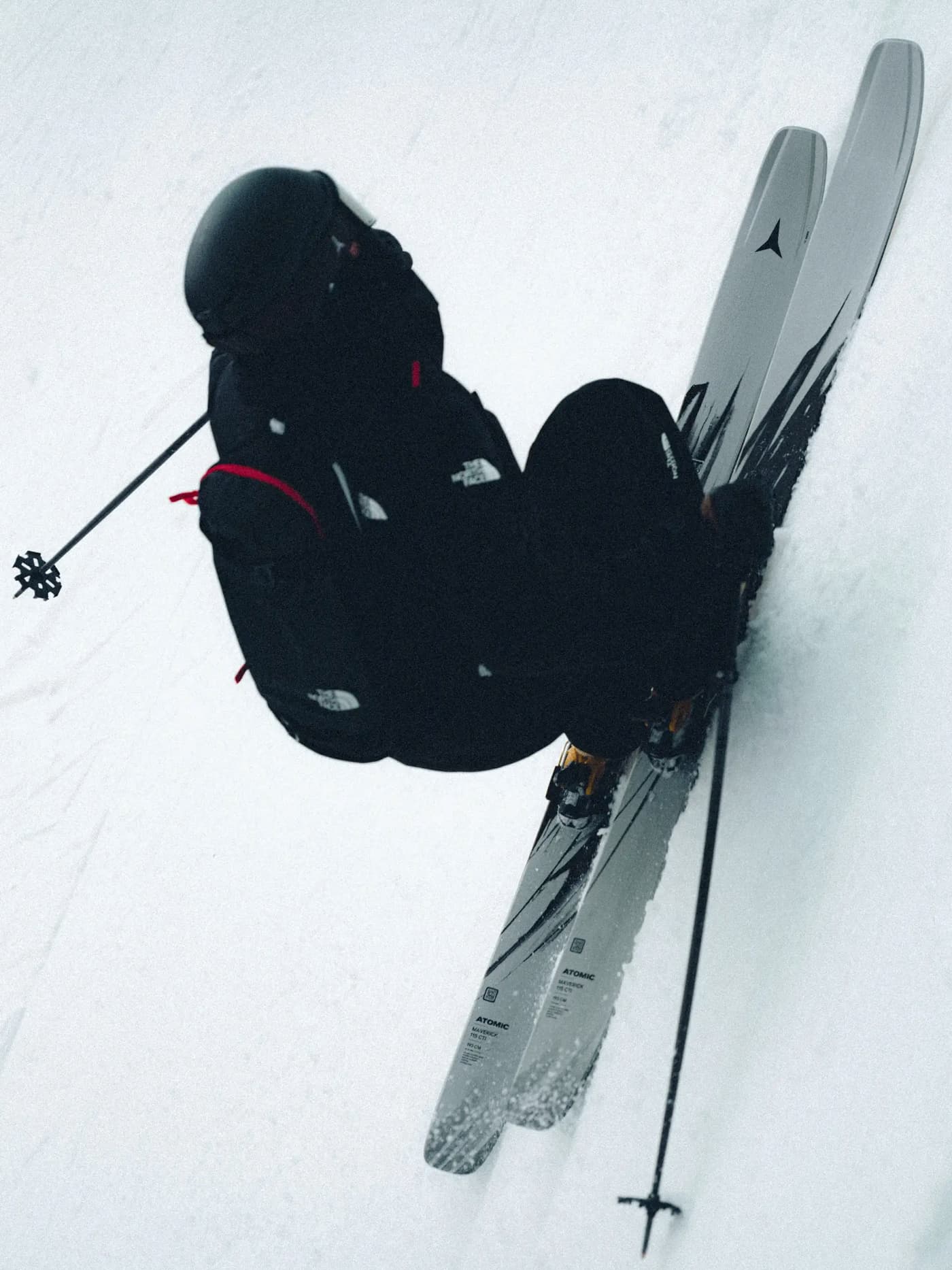 Skier in black outerwear using Atomic Maverick skis on snow, with the grey and black ski graphic visible