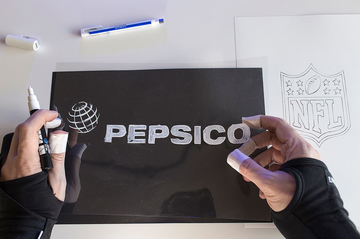 Hands drawing PepsiCo and NFL logos on tracing sheets