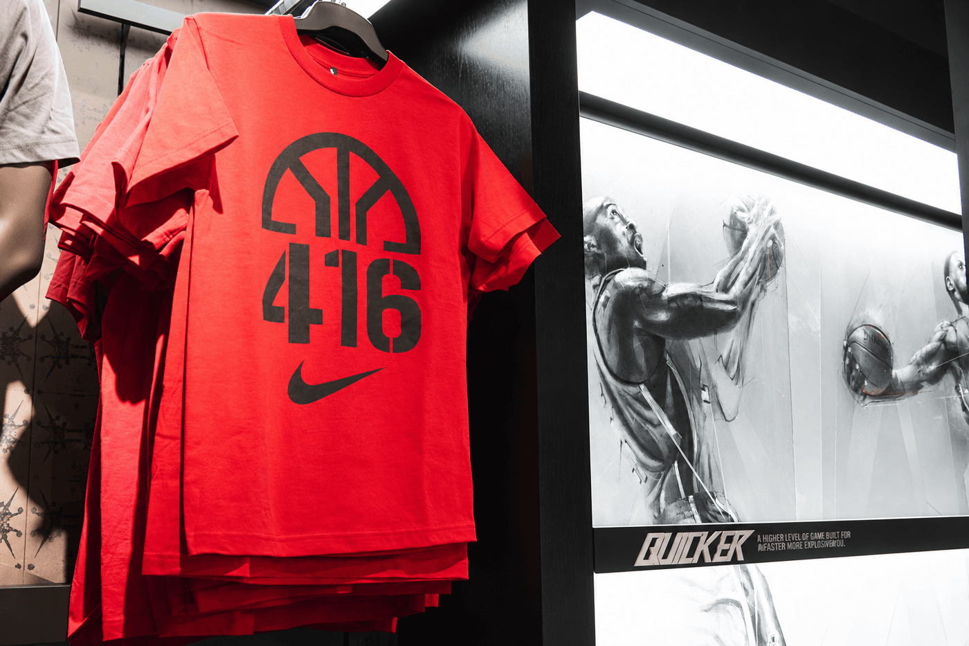 Red Nike basketball T-shirts hanging beside an illuminated House of Hoops retail wall featuring monochromatic illustrations of Kobe Bryant and LeBron James.