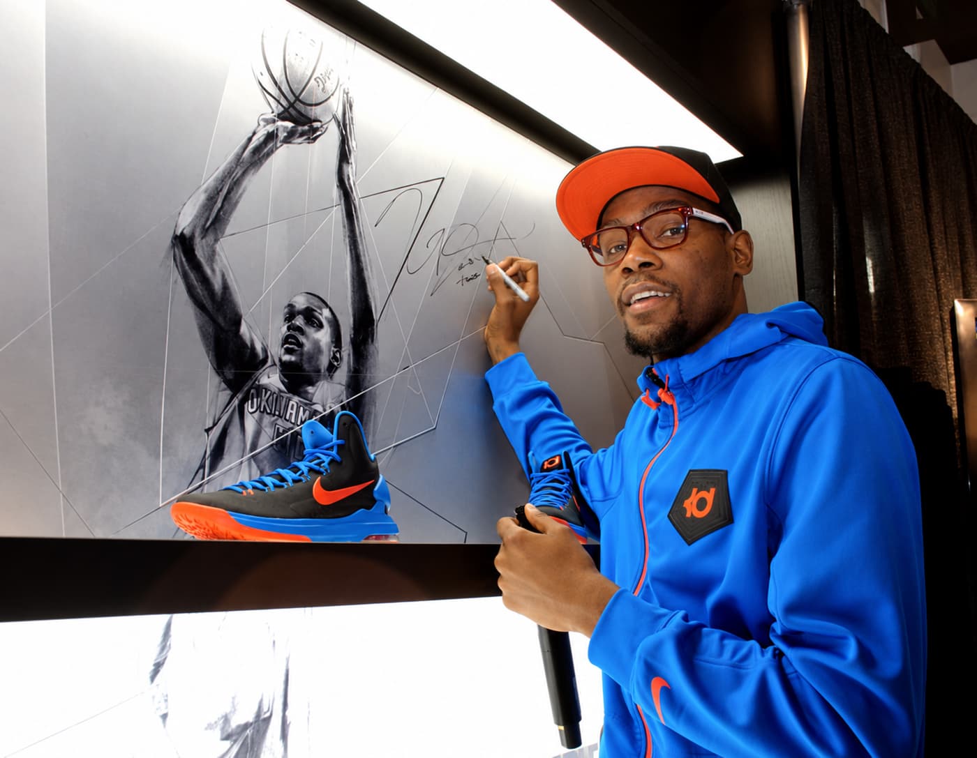 Kevin Durant signing a Nike House of Hoops retail wall featuring a monochromatic illustration of himself in an Oklahoma City Thunder uniform, with basketball shoes displayed in front.